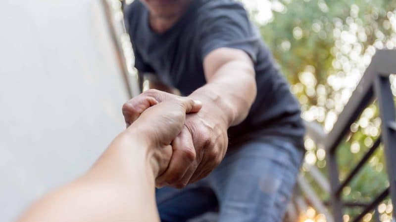 Addiction Treatment - a man helping another person by offering a hand