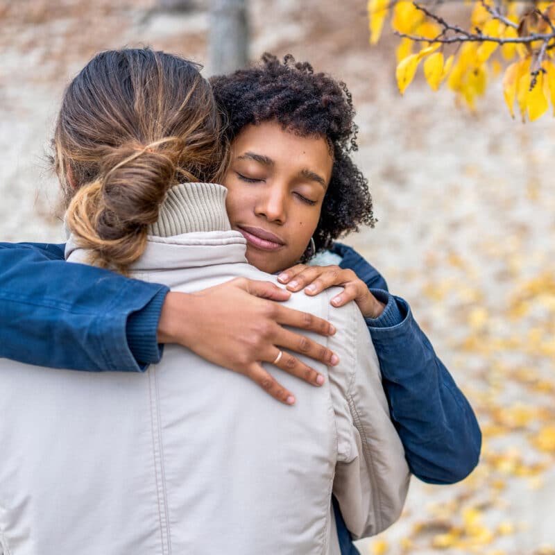 Woman hugging a loved one she wants to help get mental health addiction treatment in the park in autumn square.