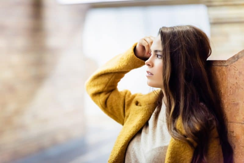 Young woman looking away and touching hair while standing near wall illustrating the link between eating disorders and mental illness.