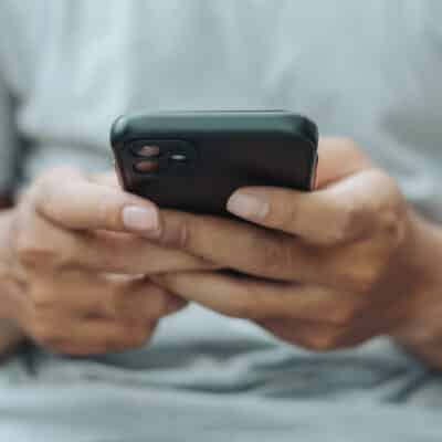 Hands of Asian man holding checking touching scrolling smartphone from bed room